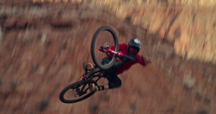 A mountain biker executes a stylish mid-air table trick while jumping in a desert setting