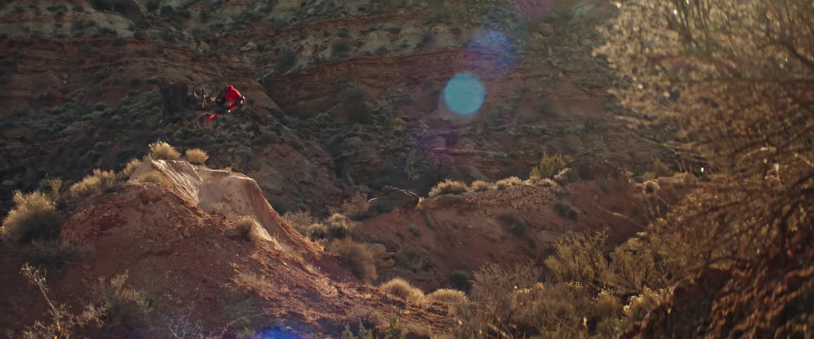 A mountain biker performs a spectacular table trick off a dirt jump in a desert canyon in dramatic slow motion
