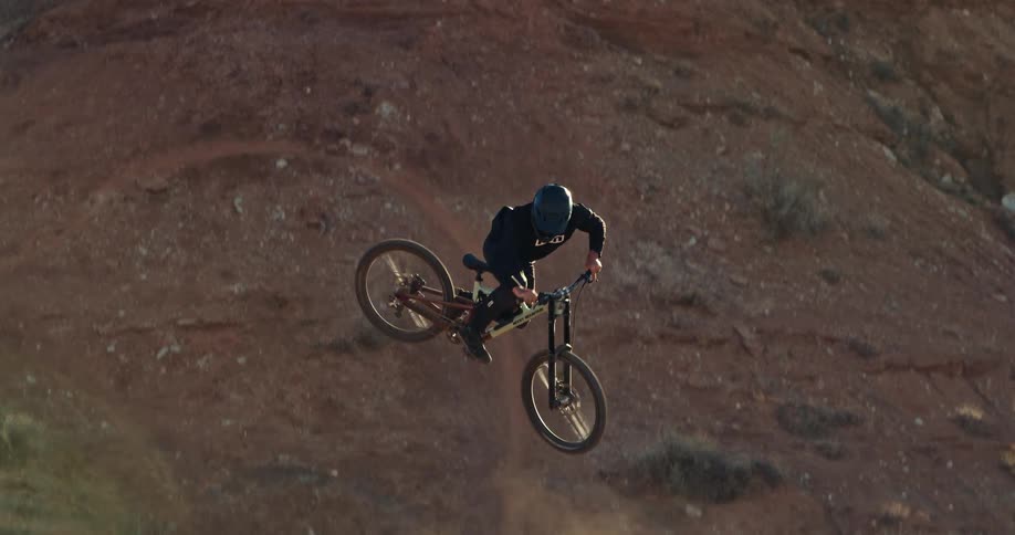 A mountain biker performs a dramatic whip off a dirt ramp in the desert in slow motion