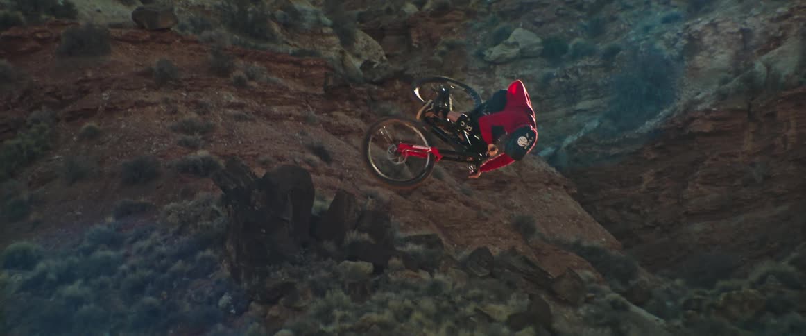 A mountain biker performs an incredibly stylish aerial table off a dirt ramp in a desert canyon in slow motion