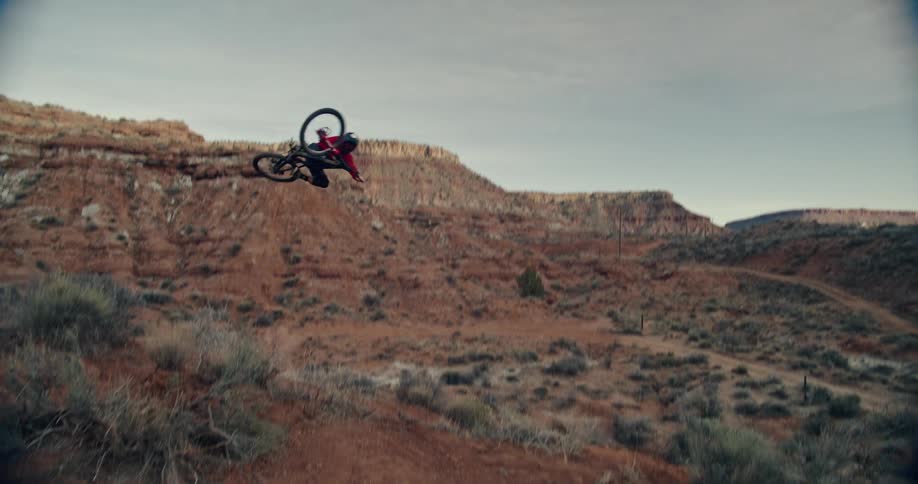 A mountain biker performs an impressive aerial table trick against a rugged desert landscape