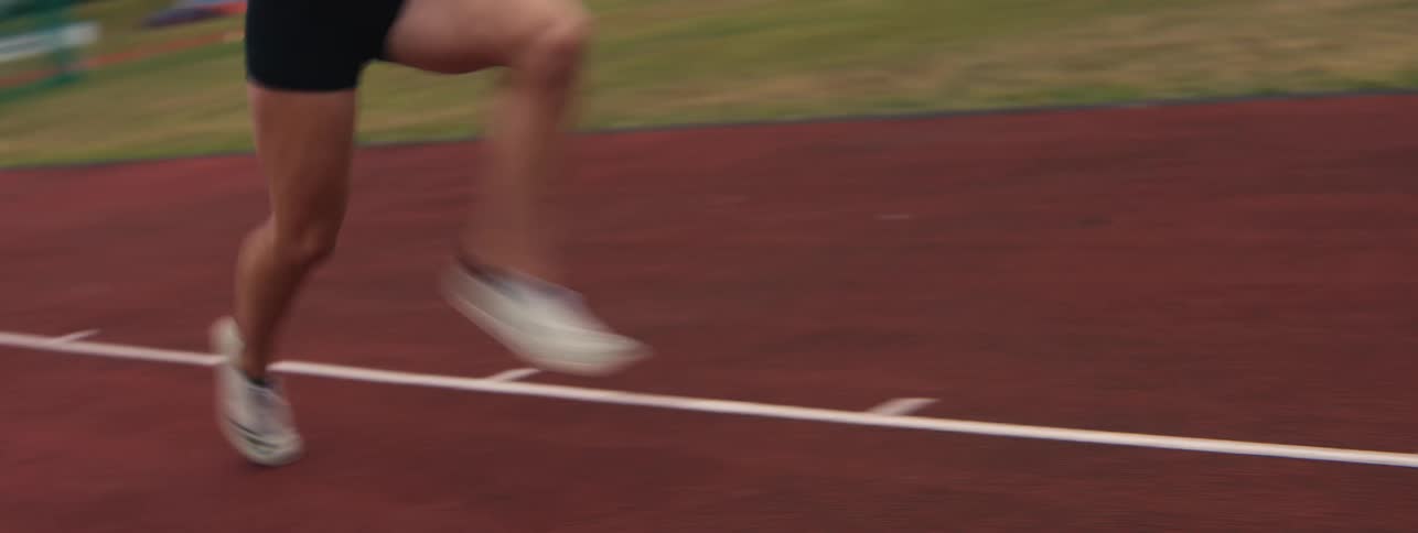 A dynamic close-up tracks the powerful legs of a female pole vaulter sprinting with a pole on a red track