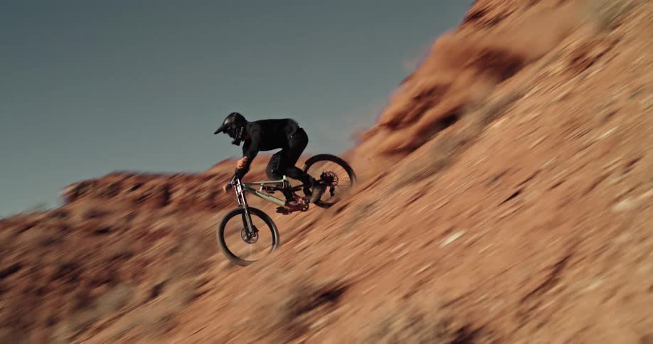 A mountain biker shreds down a steep red rock descent, kicking up a massive cloud of dust with exhilarating speed