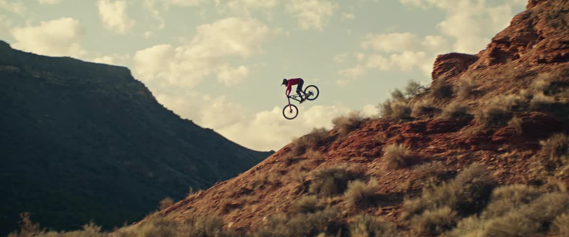 An extreme mountain biker launches off a desert cliff and soars through the air in stunning slow motion
