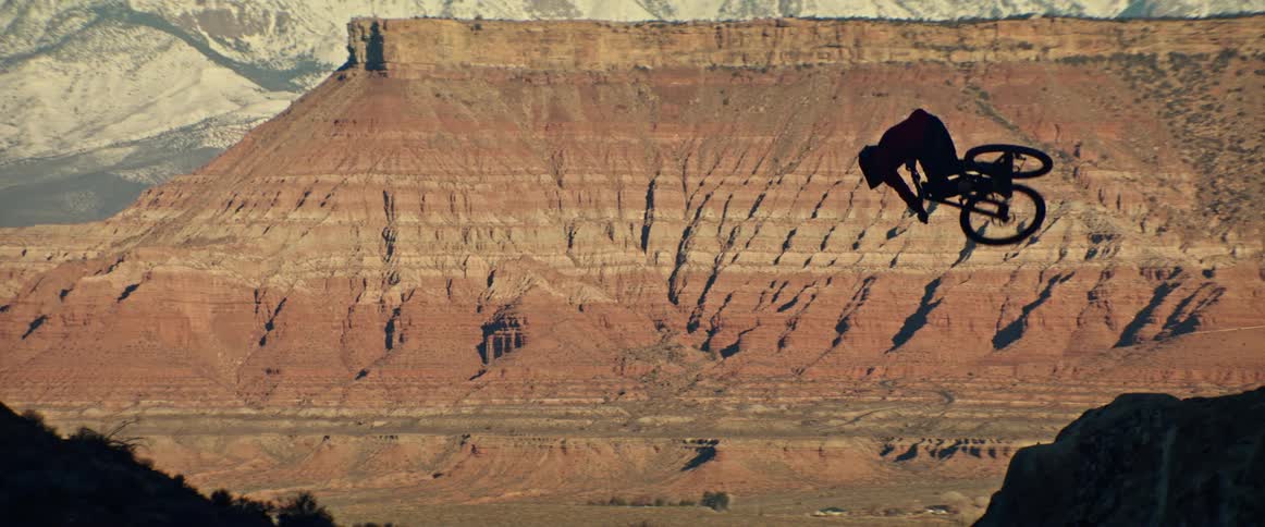 A silhouetted mountain biker performs a stylish tabletop trick in slow motion with a stunning desert butte in the background