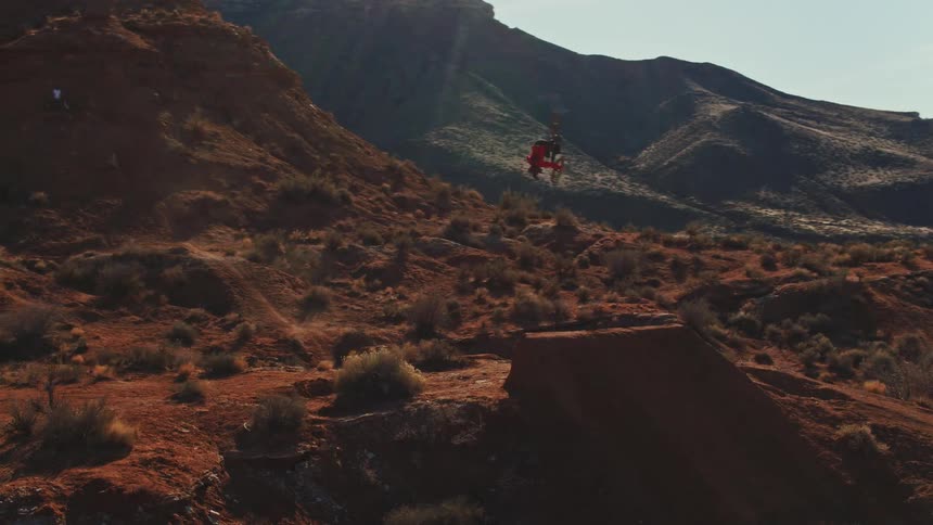 A mountain biker performs an inverted 360 spin off a dirt jump in a desert canyon