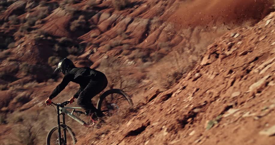 In stunning slow motion, an extreme mountain biker carves down a treacherous red rock cliff, sending a plume of dust into the desert air
