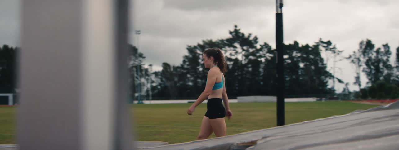 A determined female athlete walks thoughtfully across the field at an empty stadium in slow motion