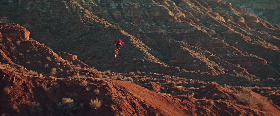 A mountain biker performs an off-axis 360 in slow motion against a stunning desert canyon backdrop during golden hour