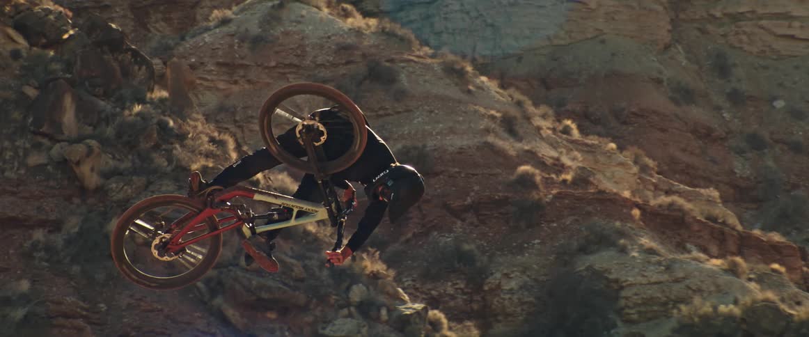 A mountain biker executes an impressive tabletop move in slow motion against a dramatic, sun-kissed canyon