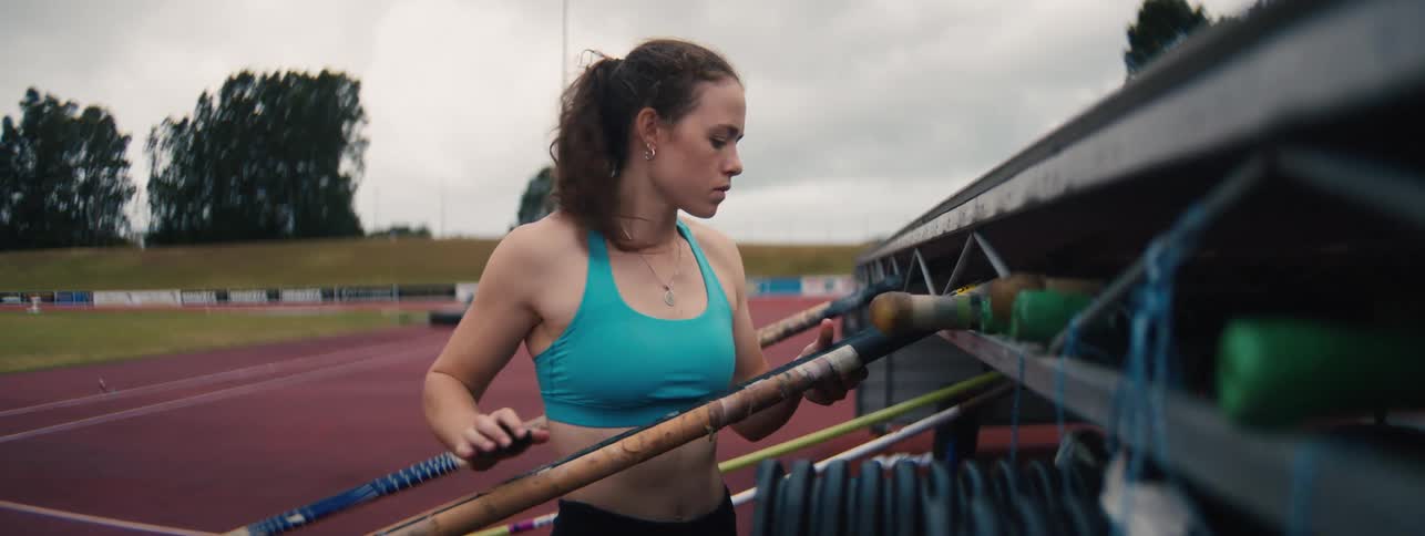A female pole vaulter carefully selects her pole and inspects the grip before training at an athletics track