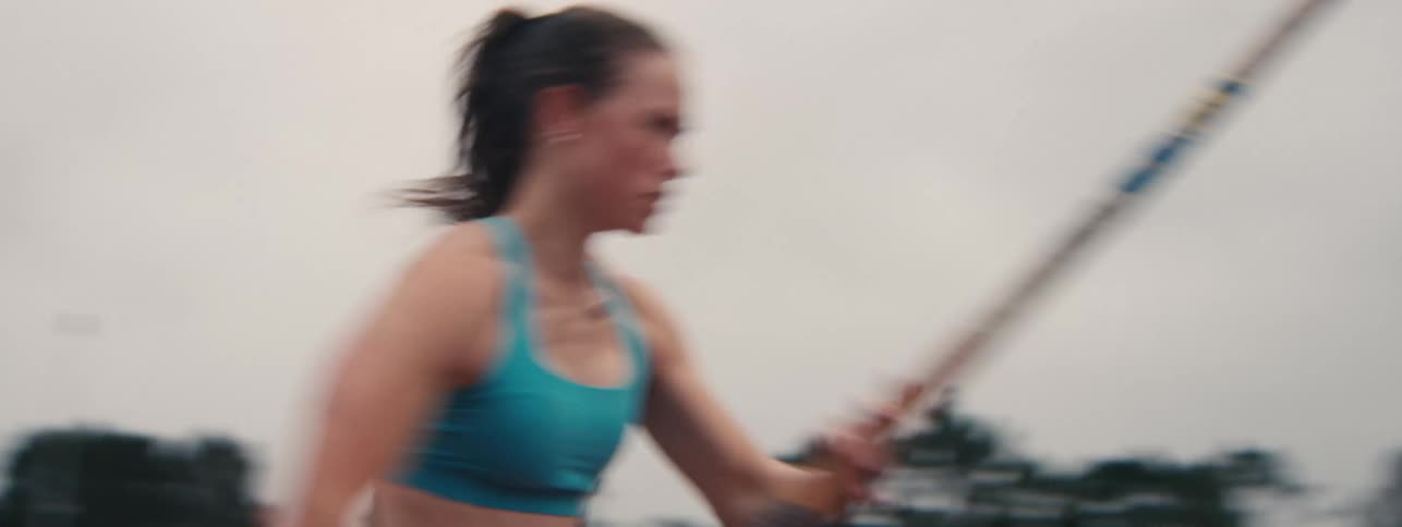 Side profile tracking shot of a focused female athlete running with a pole, preparing for a pole vault