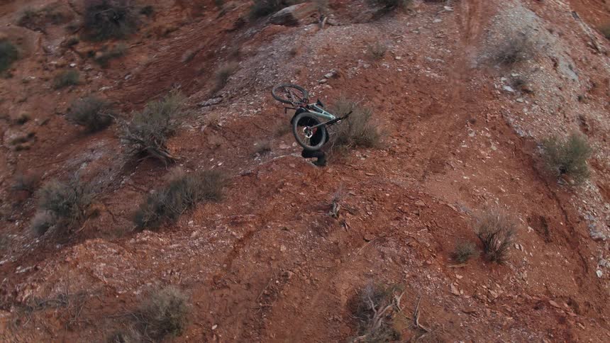 An adventurous mountain biker carries his bicycle up a steep and rugged red rock trail in a desert landscape