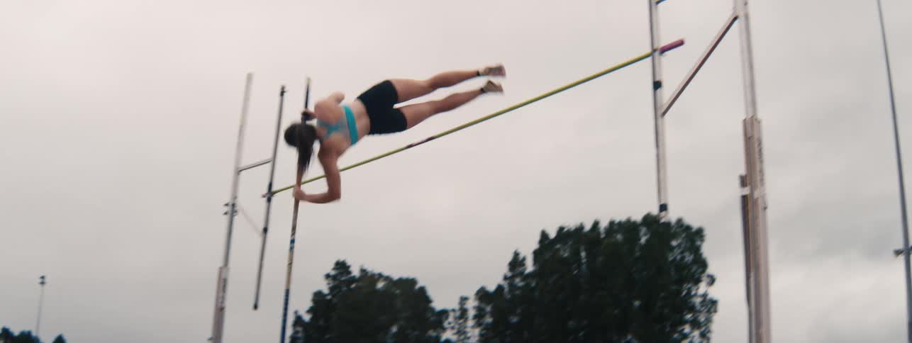 A skilled female athlete gracefully executes a pole vault in a slow-motion profile shot during a practice session