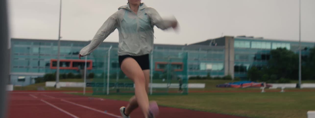 A female track and field athlete performs a running drill in slow motion on an outdoor track