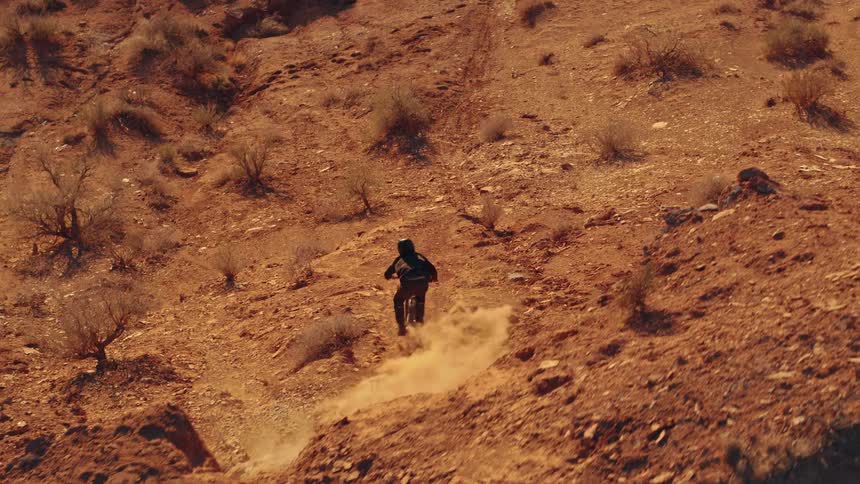 Aerial footage follows a mountain biker descend into a steep, dusty chute in the red rock desert