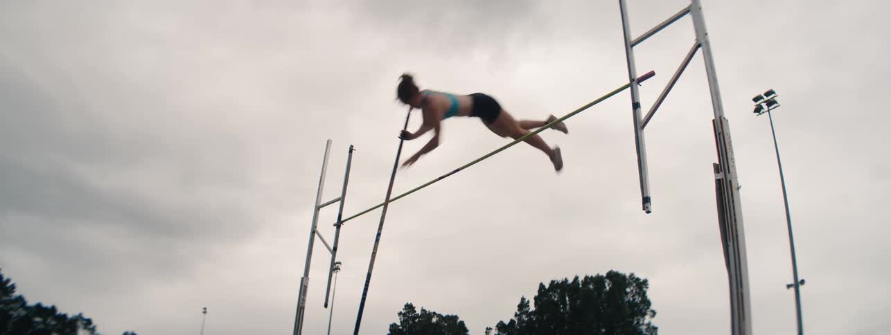 Slow motion, low angle view of a female pole vaulter successfully clearing the bar