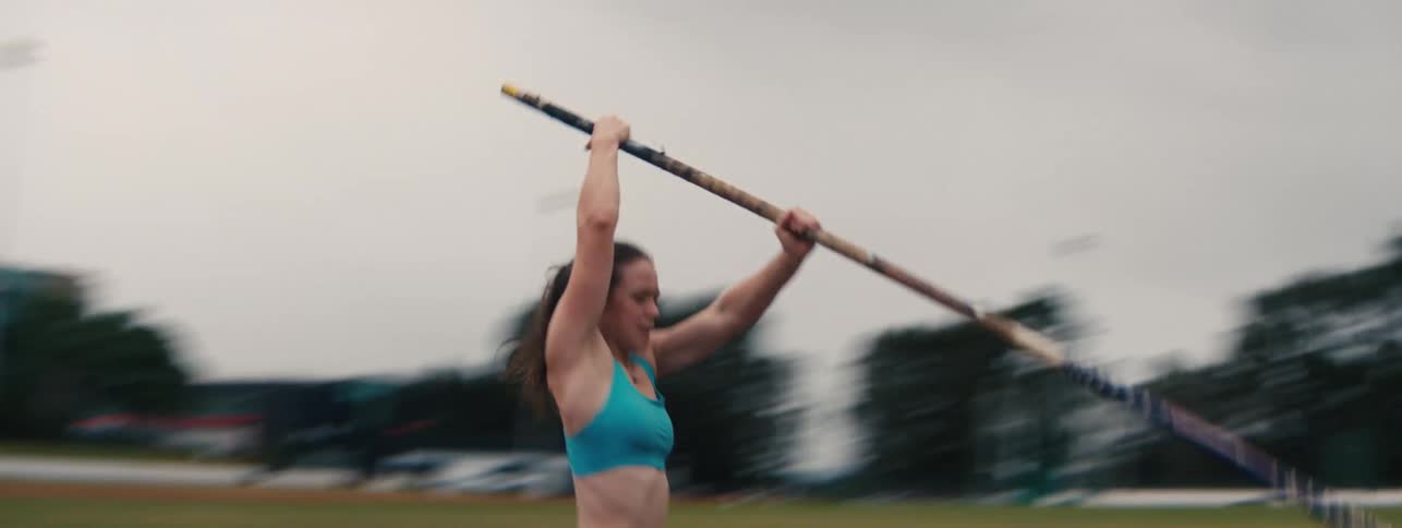 A female athlete runs with determination down an athletics track and pole vaults over the bar in slow motion