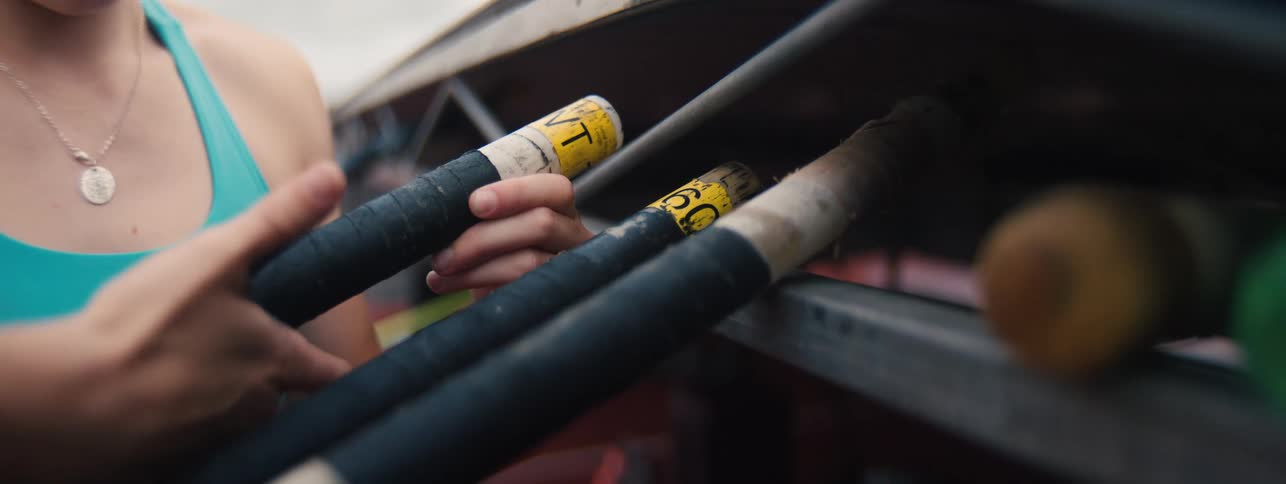 A female pole vaulter carefully selects her preferred pole from a rack before beginning her training session