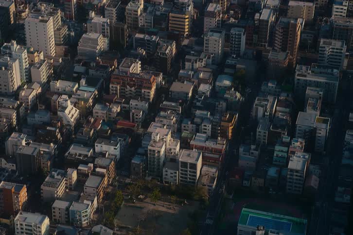 An aerial time-lapse captures long shadows moving across a dense Tokyo neighborhood during a beautiful sunset