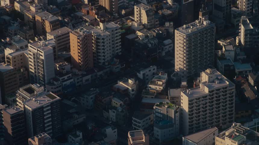 A static aerial view of a dense urban neighborhood in Tokyo during the golden hour, with cars moving below
