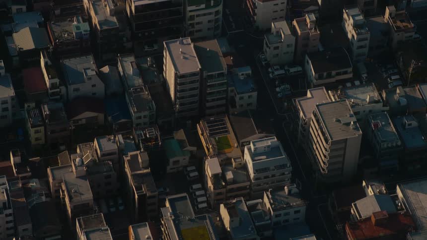 High-angle view of a quiet Japanese cityscape with long shadows stretching across rooftops at golden hour