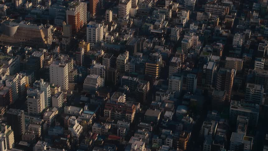 A static high-angle shot captures the golden hour sunlight slowly moving across the dense, quiet cityscape of a major metropolis