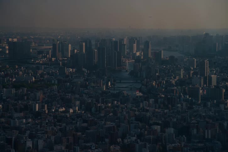 An atmospheric aerial view of a vast, hazy metropolis at dusk, with skyscrapers rising in the distance