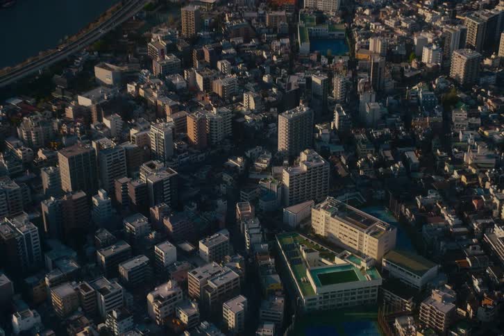 An aerial time-lapse captures the interplay of light and shadow across a dense metropolitan city during the golden hour