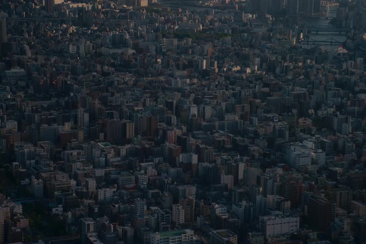 Static high-angle view of a dense city at dawn, with the rising sun casting light and shadow across the urban sprawl