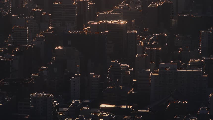 Golden hour sunlight casts long shadows across a sprawling urban cityscape from a high angle