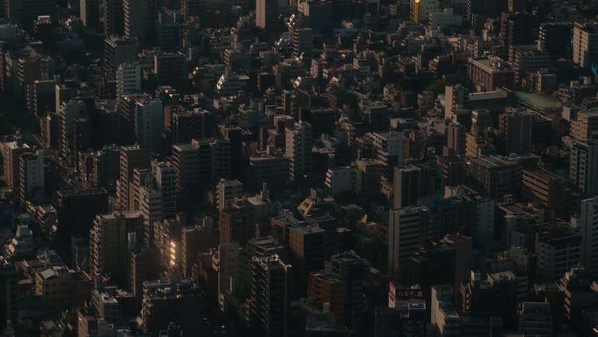 An aerial view captures the last rays of sunlight hitting the dense buildings of a sprawling city at sunset