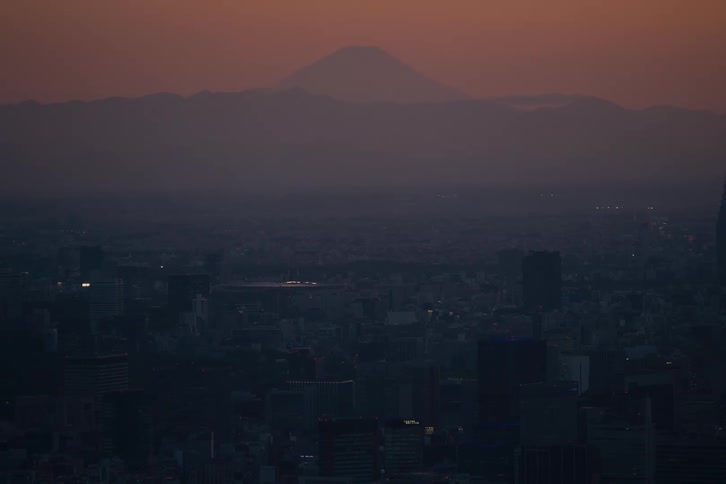 The iconic silhouette of Mount Fuji rises above the hazy Tokyo cityscape at sunset