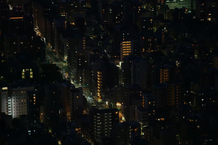 Aerial view of a city street at night with traffic flowing between tall buildings