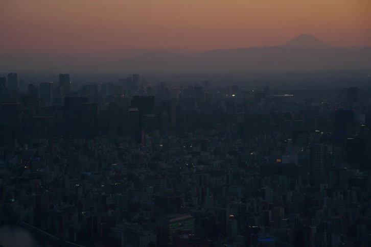 An expansive aerial view of the Tokyo cityscape as evening descends, with the iconic Mount Fuji silhouetted against the beautiful sunset sky
