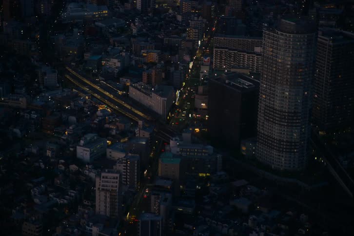 A static high-angle view captures the nighttime activity of a sprawling metropolis, with trains and cars moving through the illuminated streets