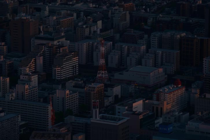 A high-angle static shot of a dense Japanese city with a prominent communication tower as the last light of day fades at dusk