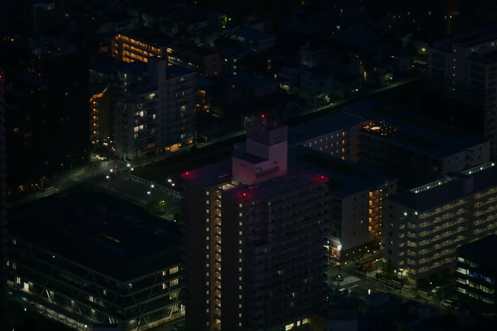 A high-angle time-lapse view shows cars driving through city streets between apartment buildings at night