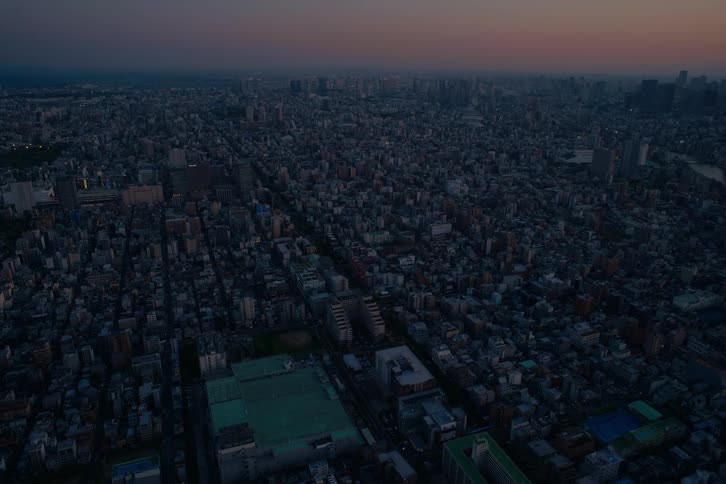 High angle time-lapse over a vast cityscape at twilight as the buildings and streets slowly illuminate for the night