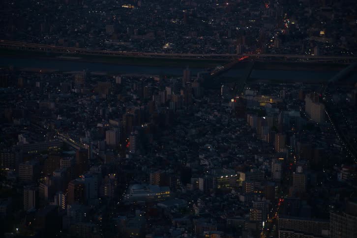 A static high-angle view captures a sprawling cityscape at twilight, with lights twinkling and traffic flowing on a distant highway