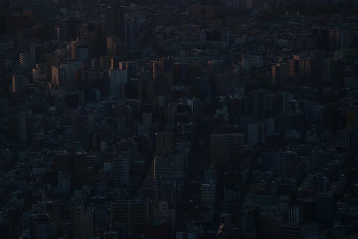 An atmospheric aerial view shows the first light of dawn hitting the buildings of a vast, dark city
