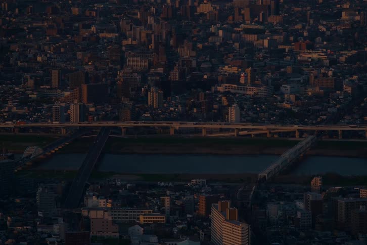Traffic flows across multiple bridges spanning a wide river in a dense urban cityscape during a dramatic golden hour sunset
