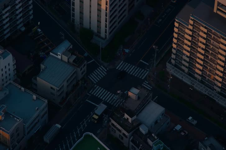 An aerial view of a quiet city intersection at dusk as vehicles and pedestrians pass through