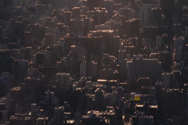 A high-angle view captures a commuter train traveling through a dense cityscape during a warm sunset