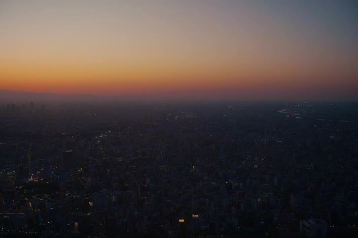The last light of sunset fades over a massive city as evening lights begin to twinkle on the horizon