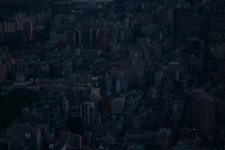 An expansive aerial shot captures the dense urban landscape of a major city as it transitions from dusk into night