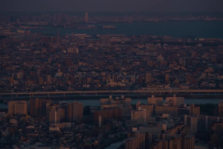 A wide aerial view of a sprawling city at dusk, with a train crossing a bridge over a wide river