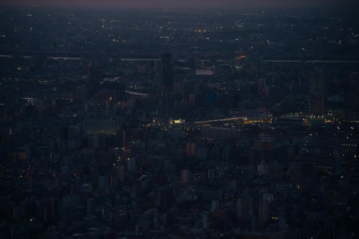 A sweeping aerial view of a dense urban cityscape at dusk with scattered lights illuminating the night