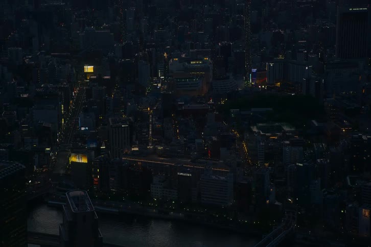 An expansive aerial view of a massive city at night, with twinkling lights illuminating the dark urban sprawl and a reflective river in the foreground