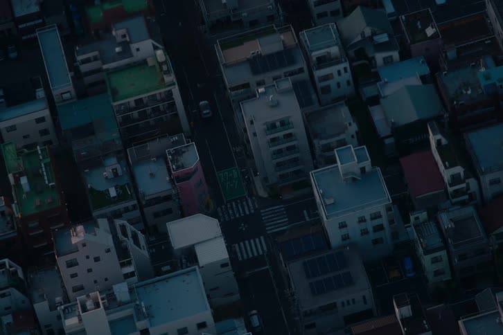 A high-angle aerial view of a quiet city street in Japan as cars pass through an intersection at dusk